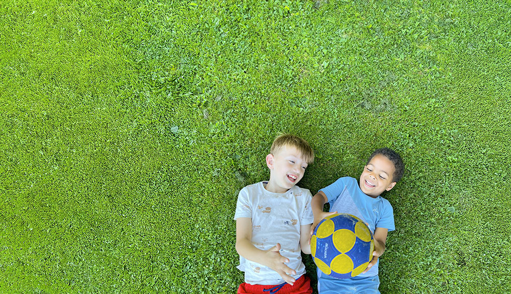 Twee jongens liggen in het gras met een voetbal.
