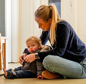 Pedagogisch professional doet de jas aan van een dreumes. 