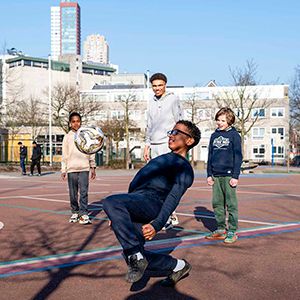 BSO-kinderen voetballen met een pedagogisch professional buiten. 