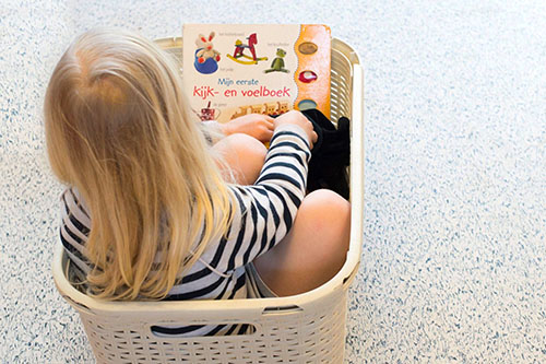 Meisje zit in wasmand van kinderopvang locatie en leest een boek.