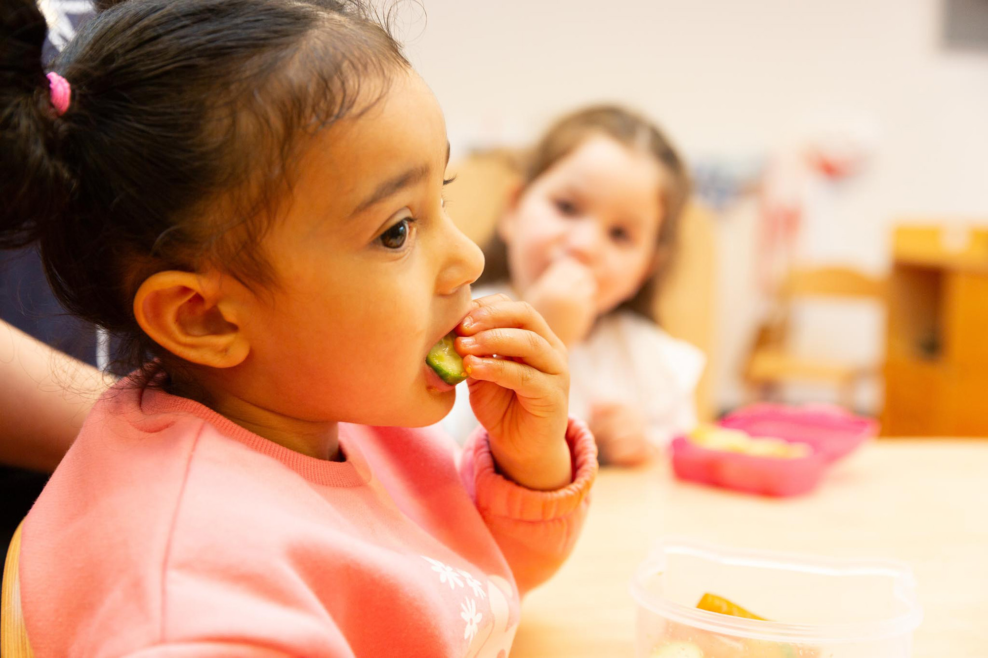 Kind eet komkommer aan tafel van peuteropvang.