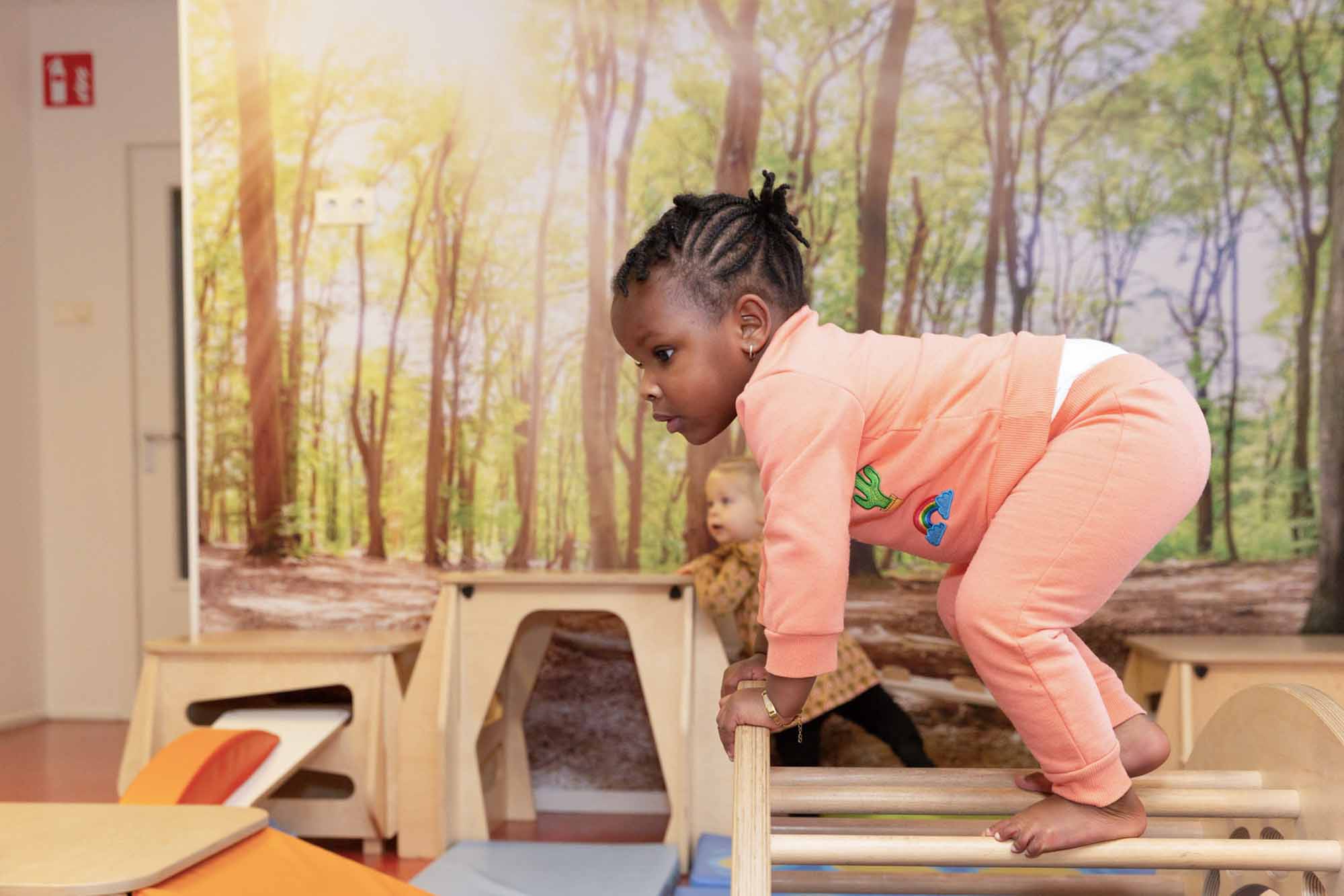 Dreumes speelt binnen bij kinderdagverblijf met houten klimtoestellen.