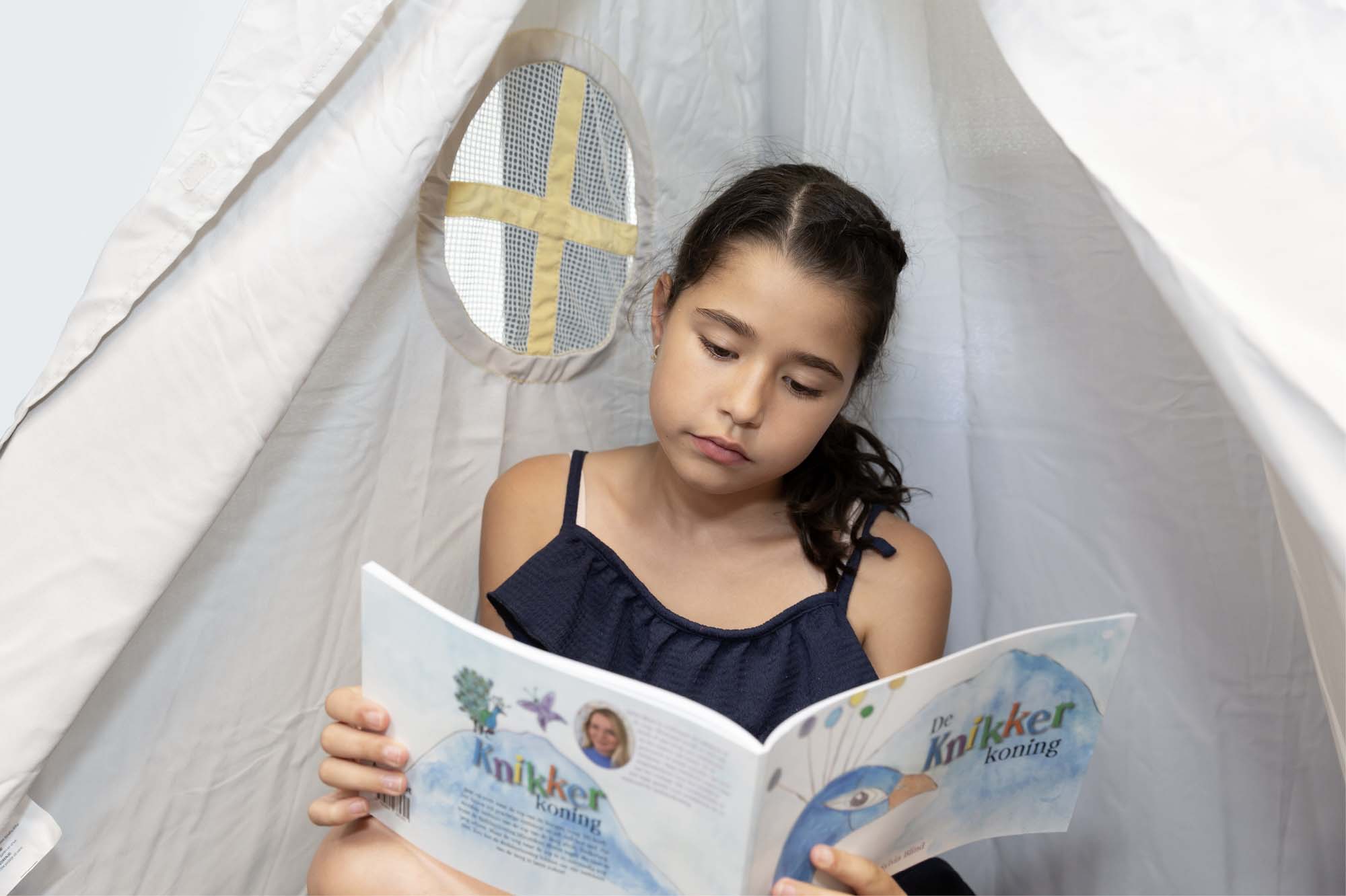 Meisje zit in een tent en leest een boek.
