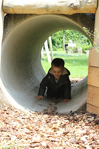 Peuter speelt buiten bij kinderopvang locatie en kruipt door een tunnel.