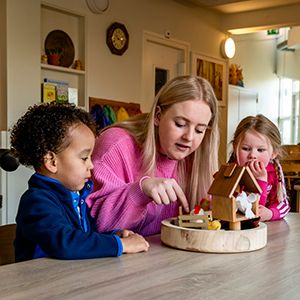 Pedagogisch professional speelt met twee peuters aan tafel van een kinderdagverblijf.