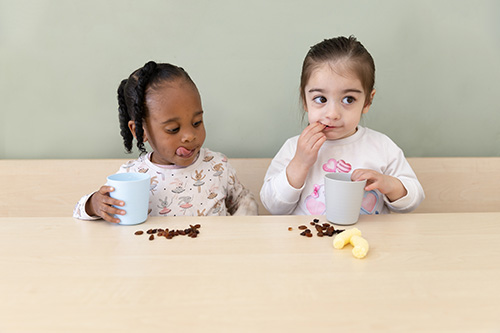 Twee peuters eten rozijntjes op de peuteropvang. 